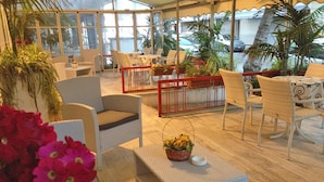 A sunlit outdoor seating area with wicker furniture, a small table with a basket, and potted plants. - Noi Due Hotel (Rimini)