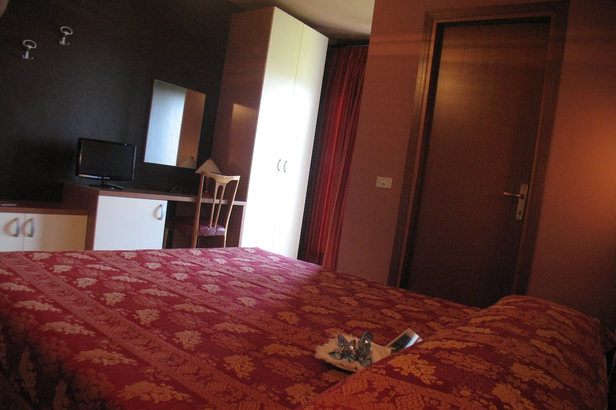Une chambre d’hôtel avec un lit, un bureau avec une télévision, une chaise et une porte.