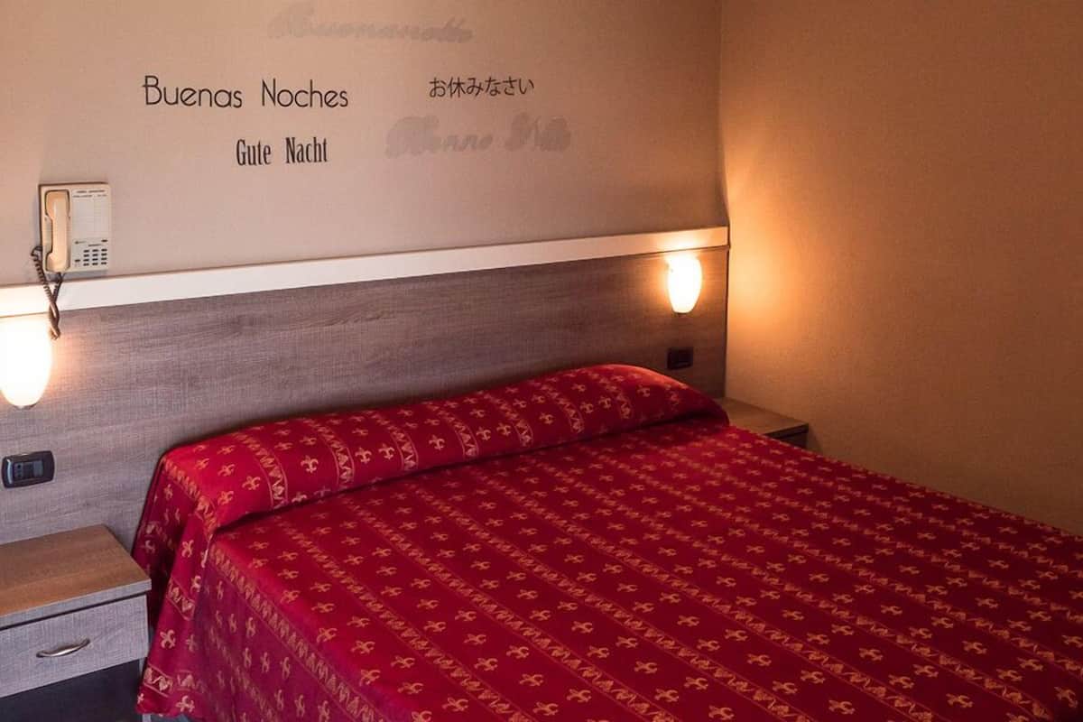 Une chambre d’hôtel équipée d’un lit, d’une table de chevet, d’un téléphone et de lampes fixées au mur.