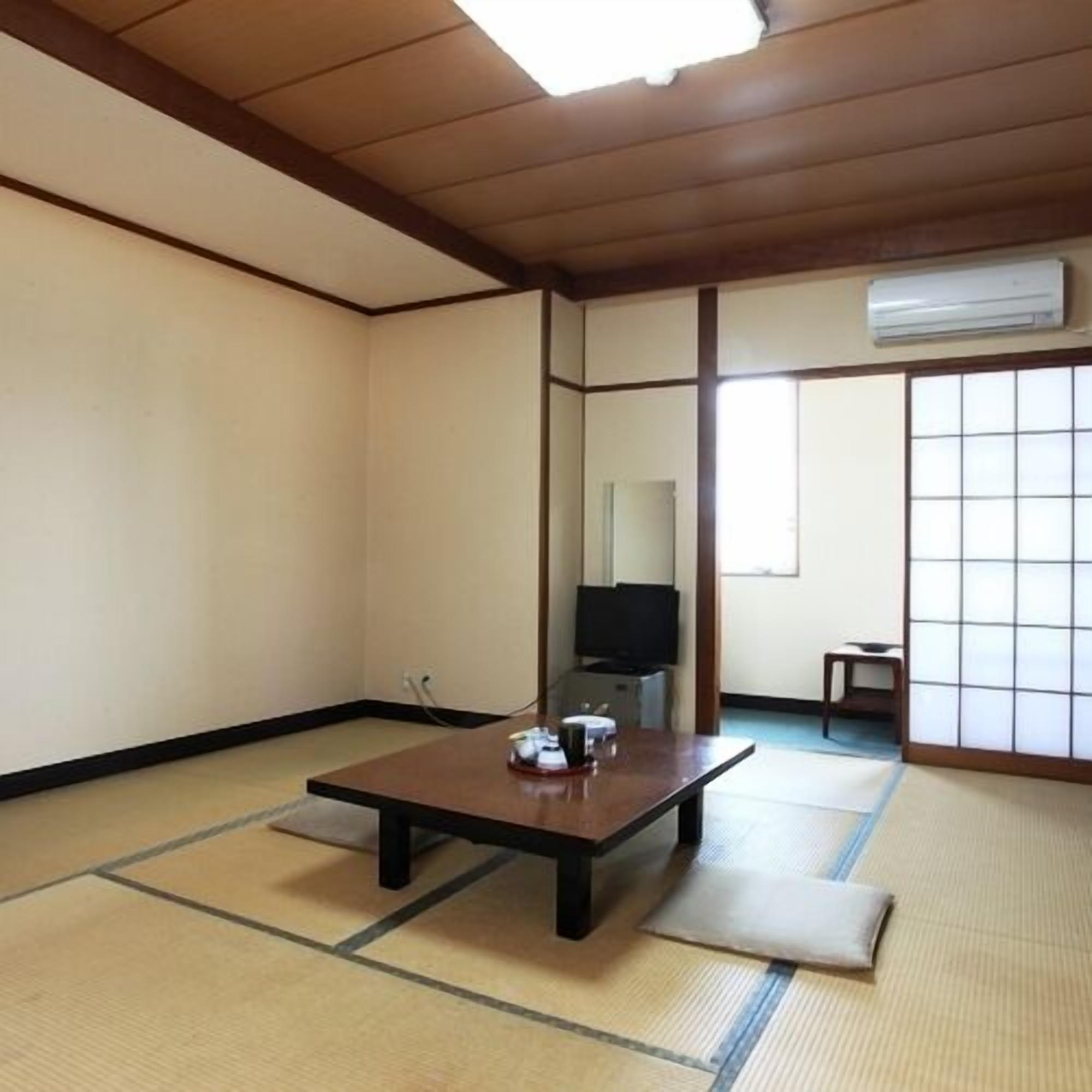 A traditional Japanese room with tatami flooring, a low table, a television, and sliding doors.
