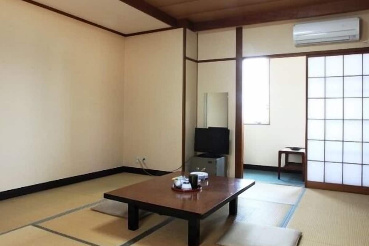 Ein traditioneller japanischer Raum mit Tatami-Böden, einem niedrigen Tisch, einem Fernseher und Schiebetüren.