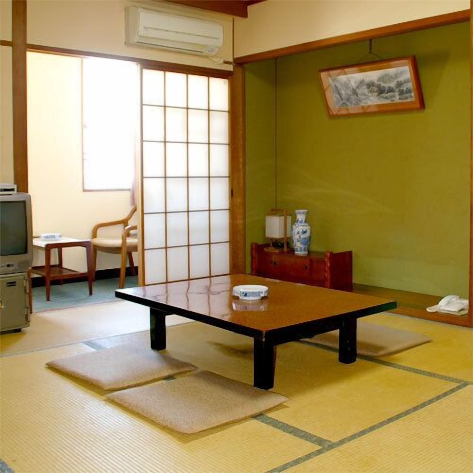 A traditional Japanese room with tatami flooring, a low table, a television, and a sliding door.