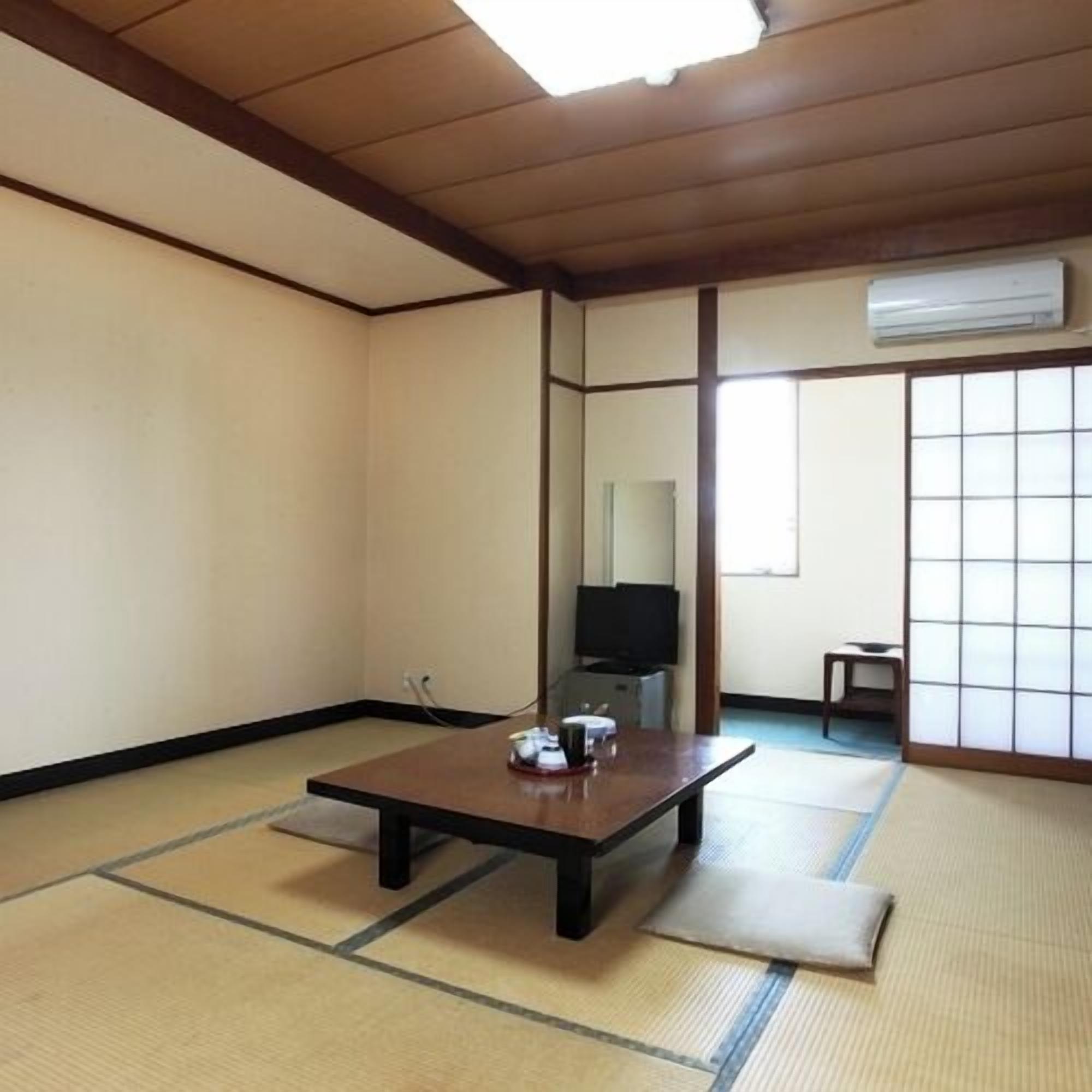 A traditional Japanese room with tatami flooring, a low table, a television, and a sliding door.