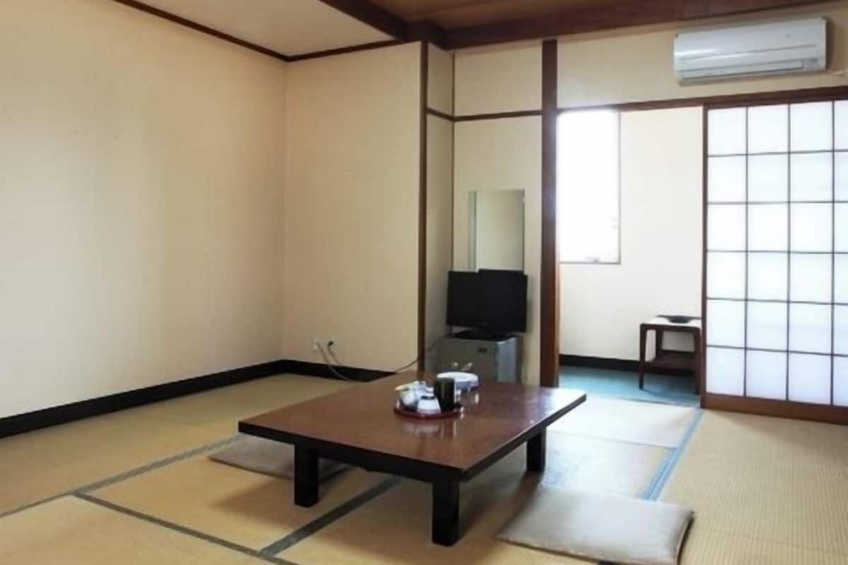 Ein traditioneller japanischer Raum mit Tatami-Böden, einem niedrigen Tisch, einem Fernseher und einer Schiebetür.