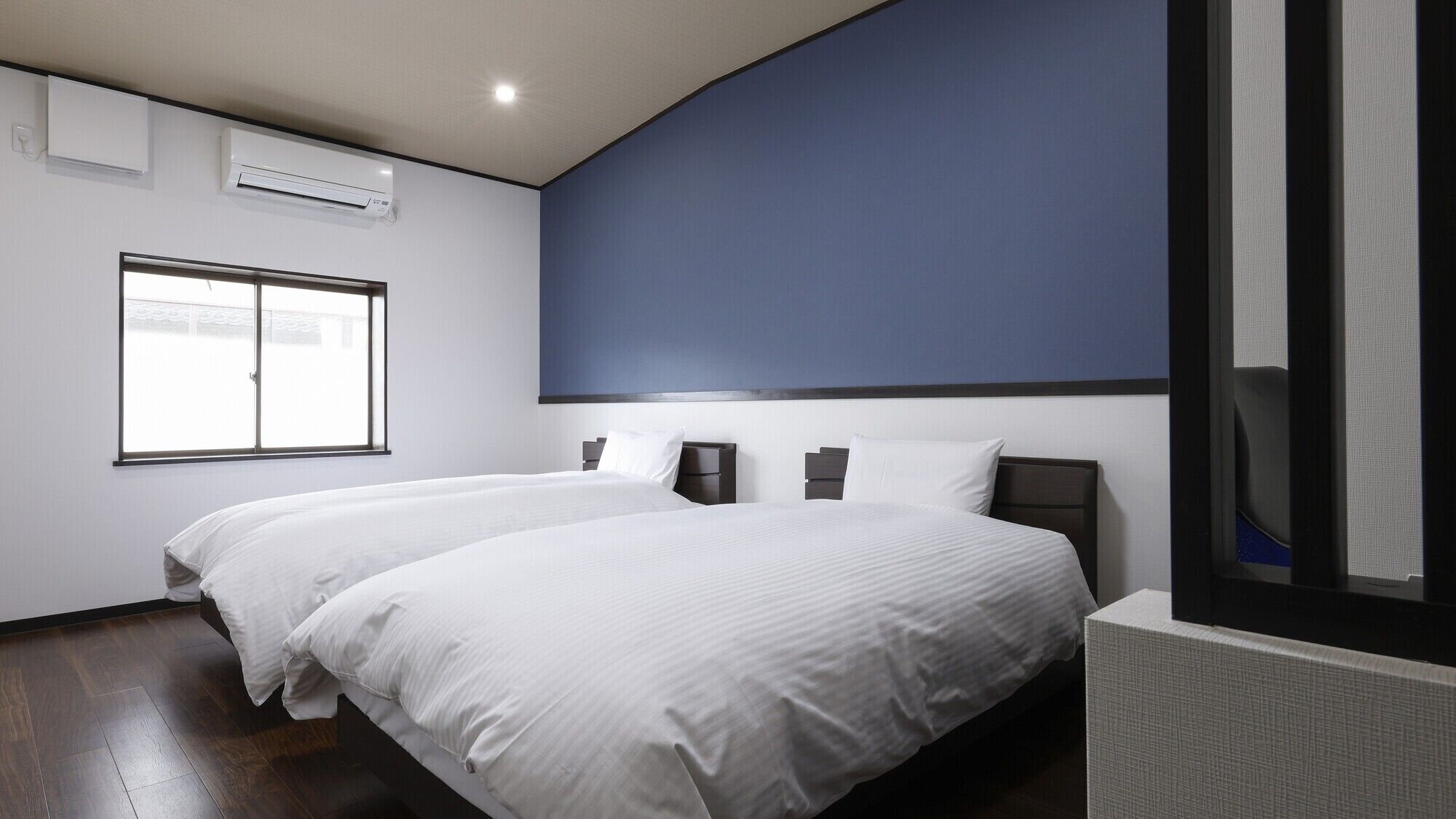 A hotel room with two beds, a large window, and a blue accent wall.