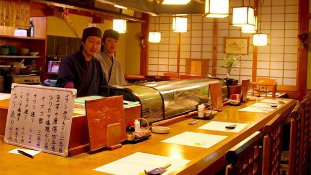 A restaurant interior with a sushi bar, wooden tables, hanging square lights, and a traditional Japanese aesthetic. - Hotel Tango Nakamuraso (Miyazu)