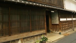 A traditional wooden building with a tiled roof, a wooden fence, and a small garden area with potted plants. - Hotel Tango Nakamuraso (Miyazu)