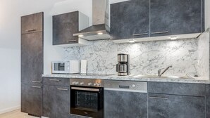 A modern kitchen with grey cabinetry, a built-in oven, a microwave, and a coffee maker. - Apartment 5 (ID 171), Germany (Sankt Peter-Ording)