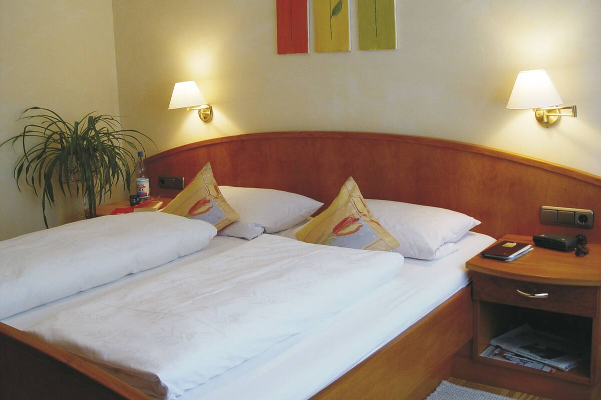 A double bed with white linens, two bedside tables with lamps, and a wall with three framed pictures.