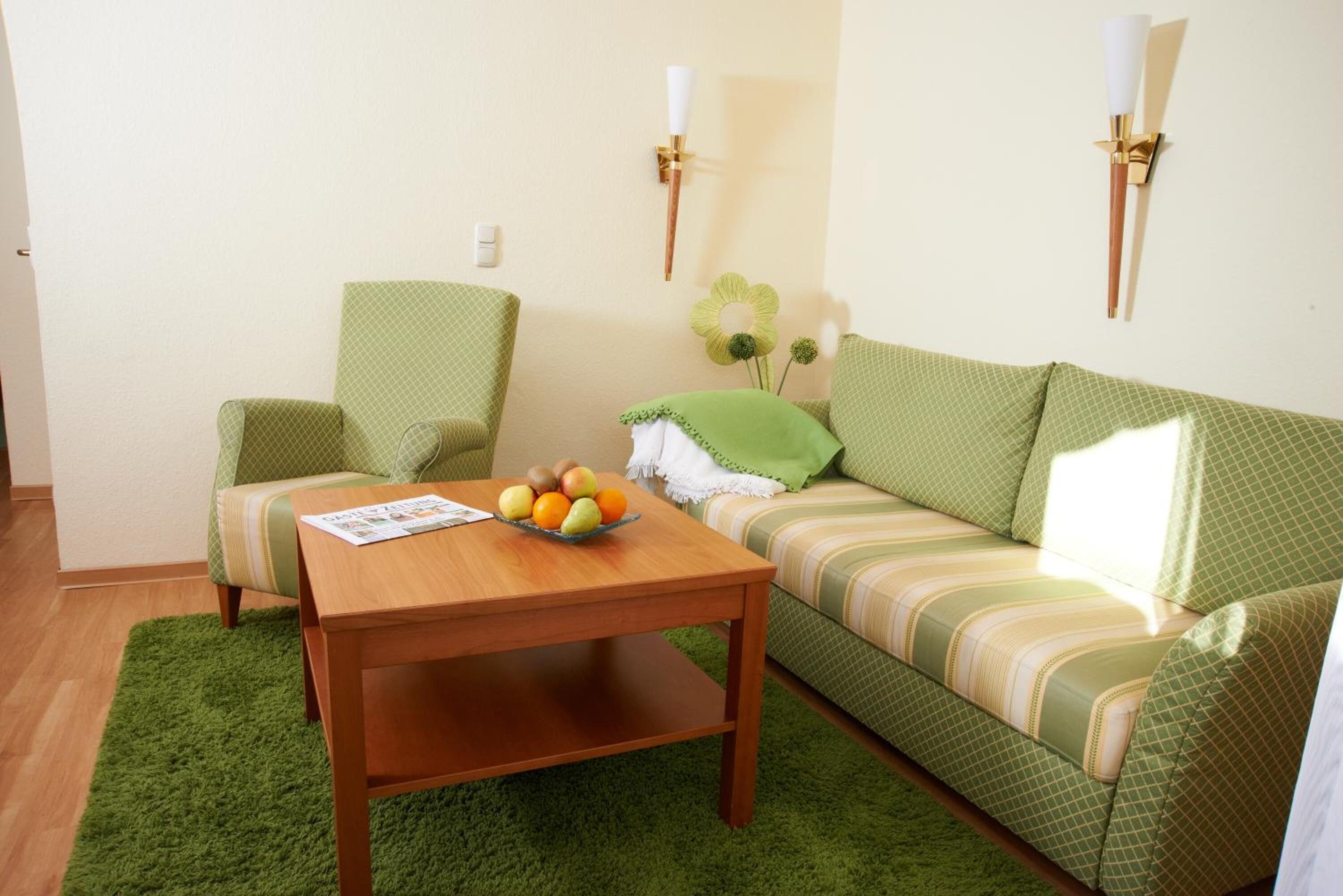 A living room with a green sofa, a wooden coffee table with fruits, and two wall-mounted lamps.