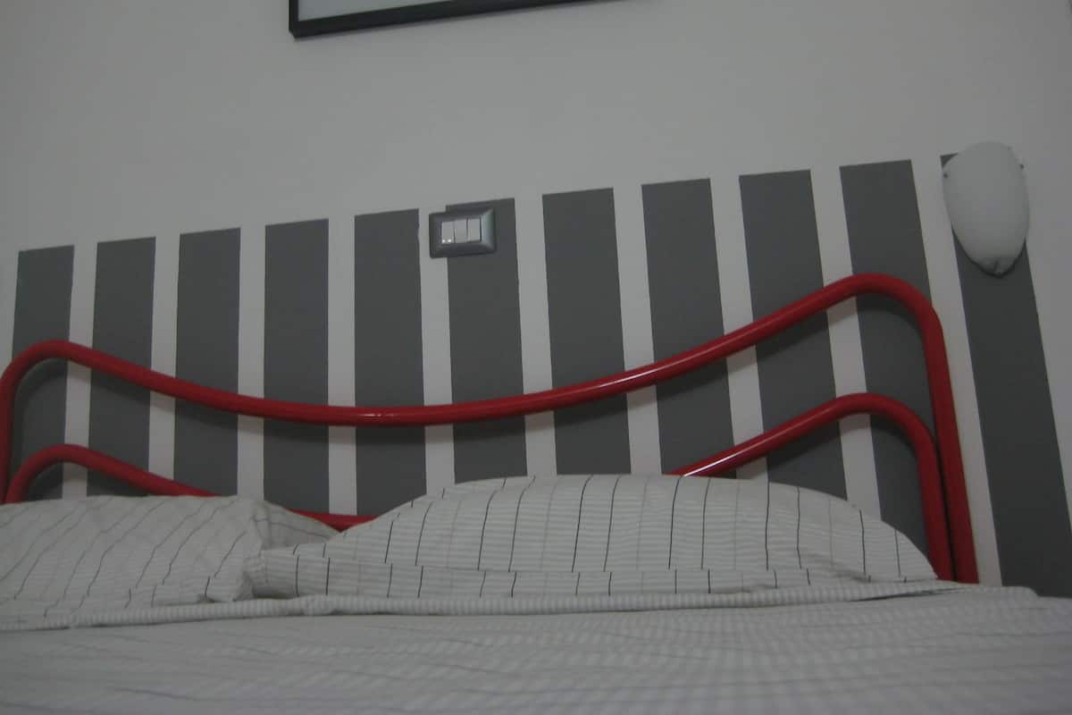 Un lit avec une tête de lit à rayures, une lampe de chevet et un tableau encadré accroché au mur.