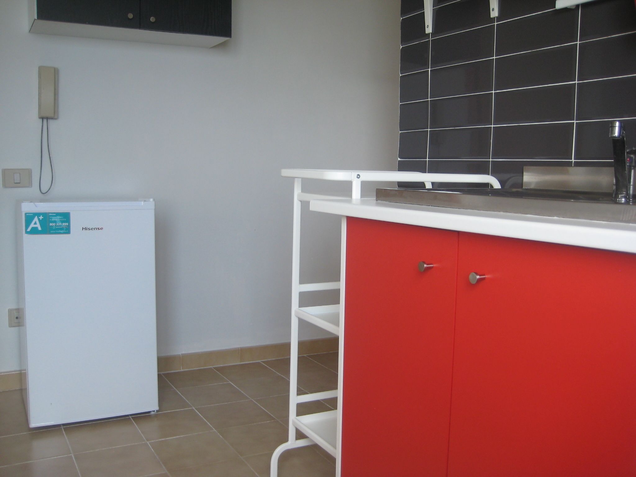 A compact kitchen with a white refrigerator, a red cabinet, and a black tiled backsplash.