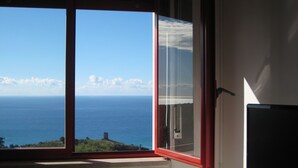 Habitació amb una finestra gran que ofereix vistes al mar i a la costa llunyana.
