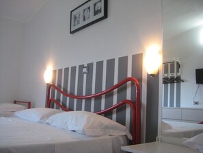 A hotel room with a striped headboard, a bed with white linens, a bedside table, a nightstand, a wall-mounted TV, and a framed picture above the headboard. - Residence San Antonio (Camerota)