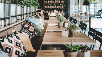 A restaurant with wooden tables and benches, potted plants, and a long counter.