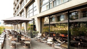 Un espace extérieur aménagé avec des tables et des chaises, une zone couverte avec des parasols, et un bâtiment doté de grandes fenêtres.