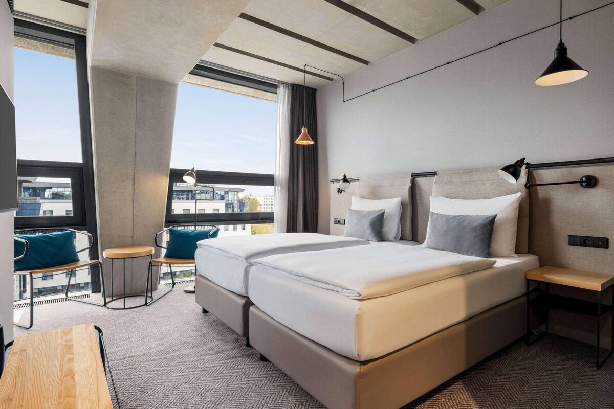 Une chambre d’hôtel avec un grand lit, un bureau, une chaise, une petite table et une vue sur la ville.