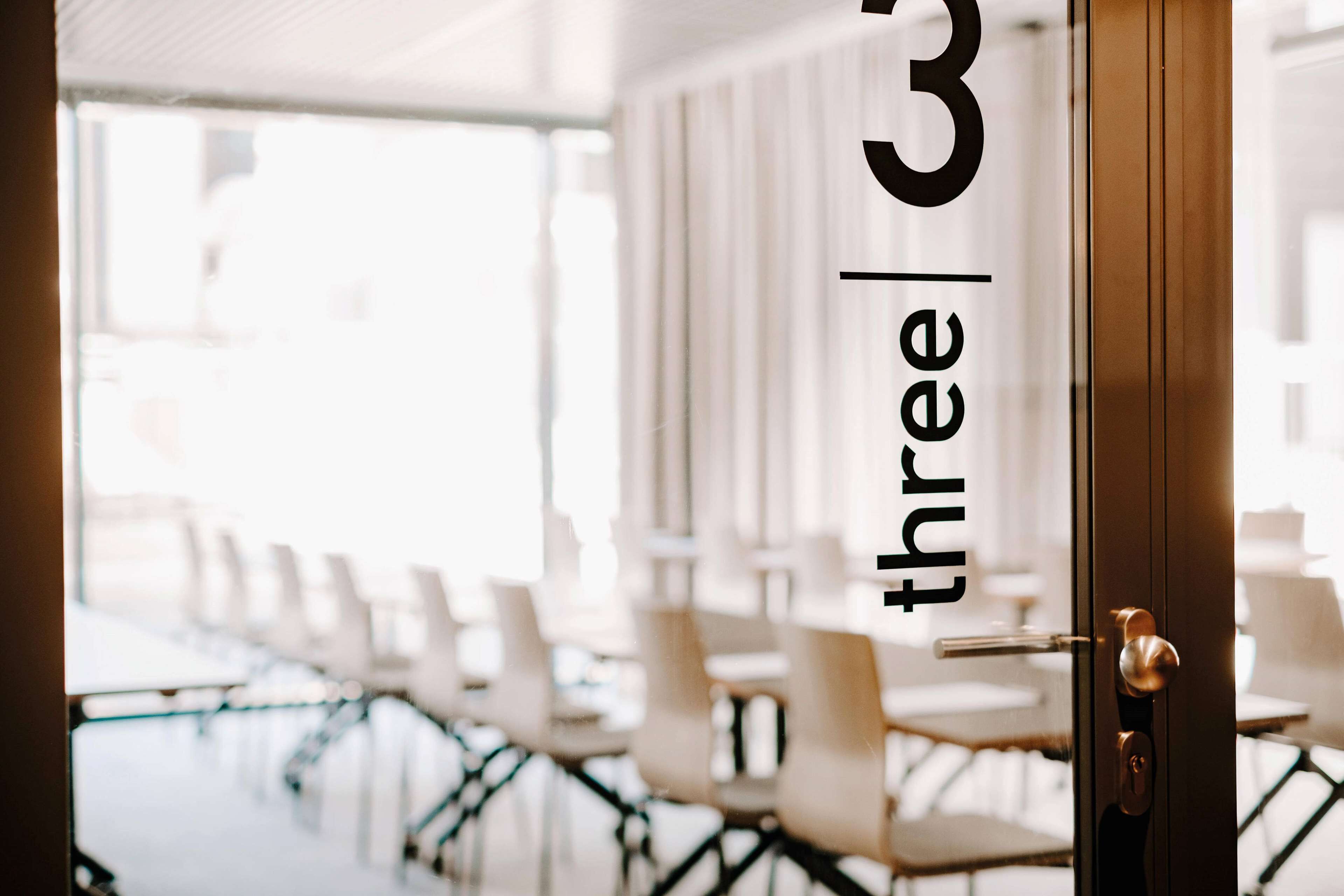 A conference room with rows of chairs and a door with the text "three | tree" on it.