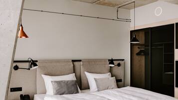 Una habitación de hotel moderna con una cama grande, una mesita de noche, una pequeña mesa redonda con una botella y un armario.
