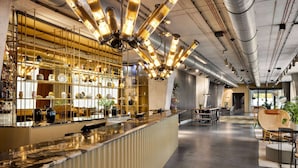 Een moderne bar met een lange toonbank, planken met decoratieve objecten, en een zithoek met tafels en stoelen.