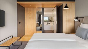 Een moderne hotelkamer met een groot bed, een houten bankje, een bureau en uitzicht op de badkamer.