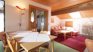 A room with a wooden dining table, chairs, a sofa, and a red carpet. - Appartements Reiter am See (Inzell)