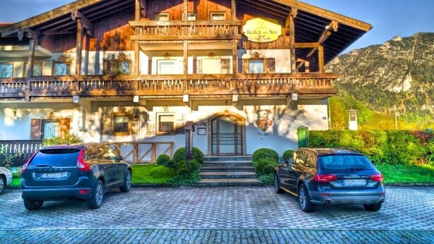A traditional wooden chalet with a balcony, a sign reading "Reiter am See," and two cars parked in front. - Appartements Reiter am See (Inzell)