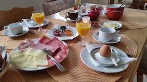 Uma mesa de pequeno-almoço com pratos de presunto, queijo e ovos, juntamente com copos de sumo de laranja e compota.