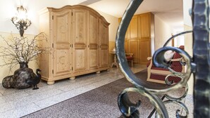 A spacious room with a large wooden cabinet, a decorative vase with branches, and a patterned chair. - Appartements Reiter am See (Inzell)