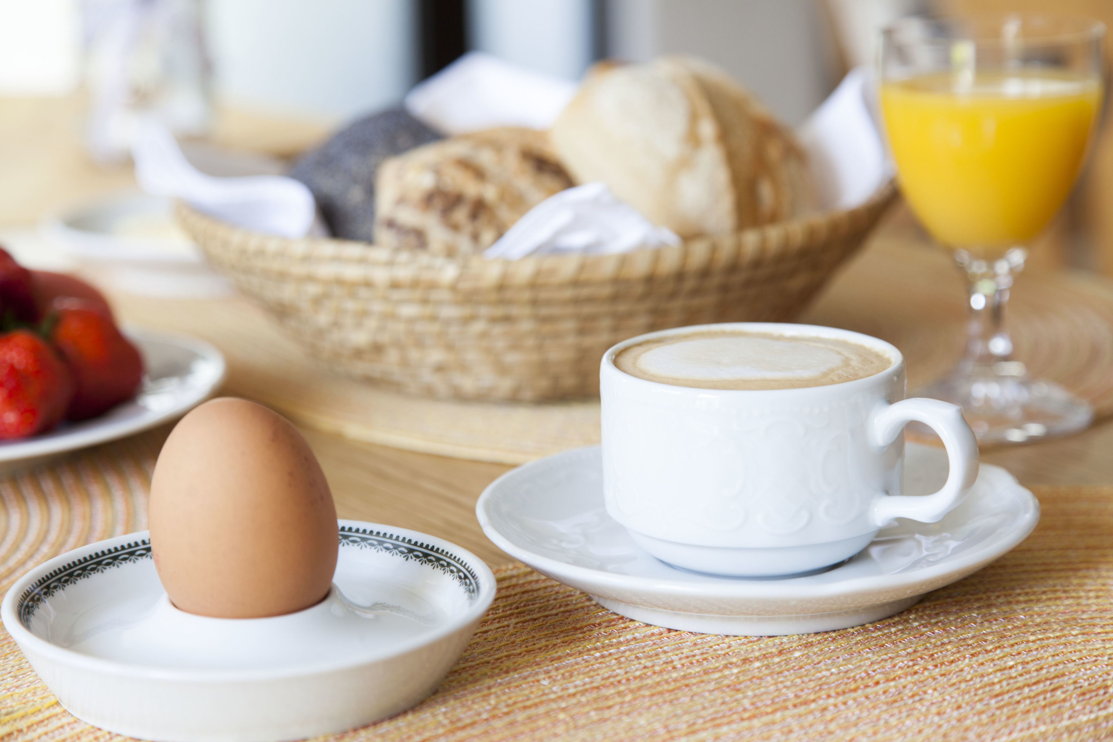 A breakfast setting with a cup of coffee, a plate with an egg, a basket of bread, and a glass of orange juice.