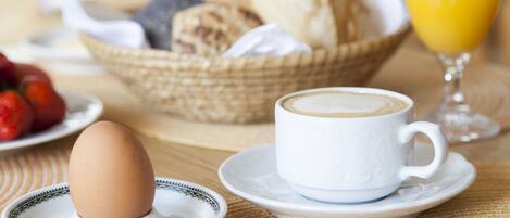 A breakfast setting with a cup of coffee, a plate with an egg, a basket of bread, and a glass of orange juice.
