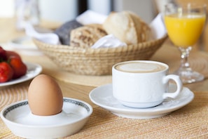 Disposição para o café da manhã, com uma xícara de café, um prato com ovo, uma cesta de pão e um copo de suco de laranja.