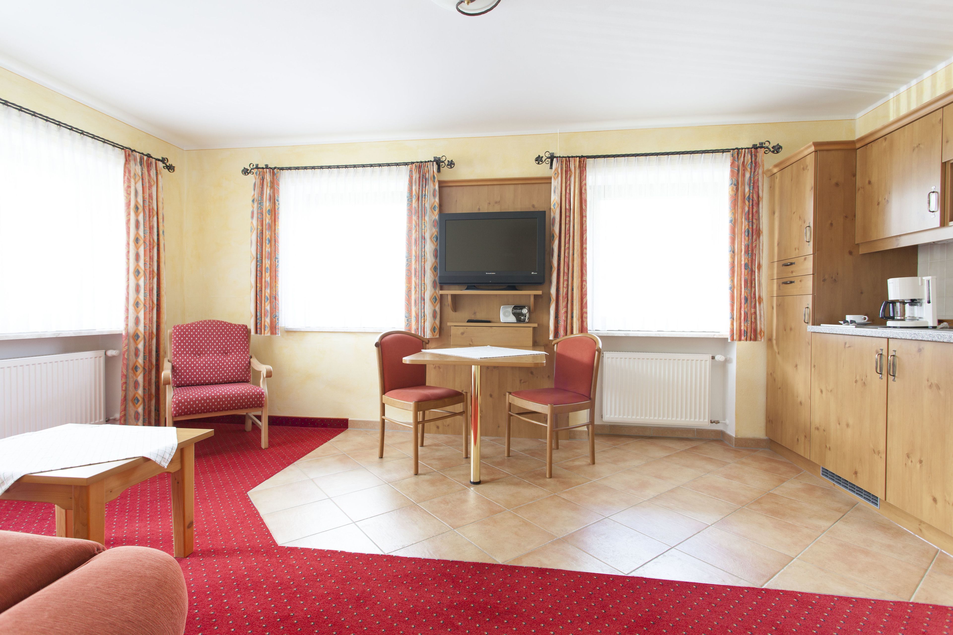 Een kamer met een eettafel, twee stoelen, een televisie en een kitchenette.