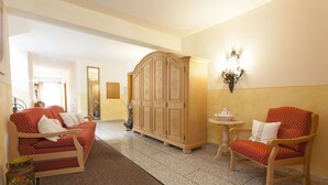 A hotel room with a red sofa, a wooden cabinet, and a small table with a lamp. - Appartements Reiter am See (Inzell)