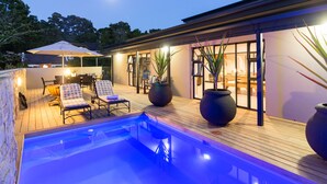 Uma área de piscina moderna ao ar livre, com espreguiçadeiras, deck de madeira e grandes vasos de plantas.
