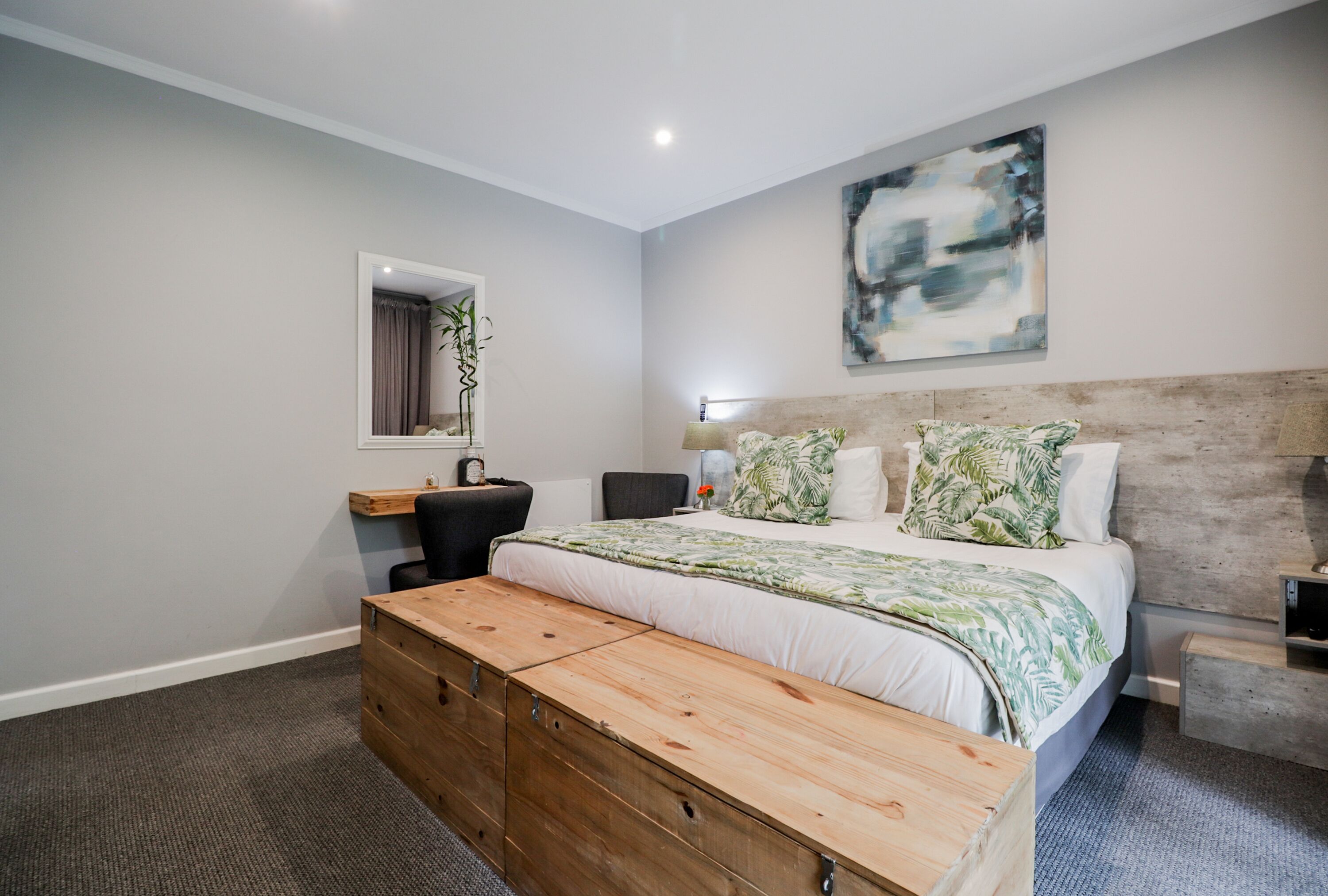 A modern bedroom with a large bed, a wooden bench, a desk, and a mirror.