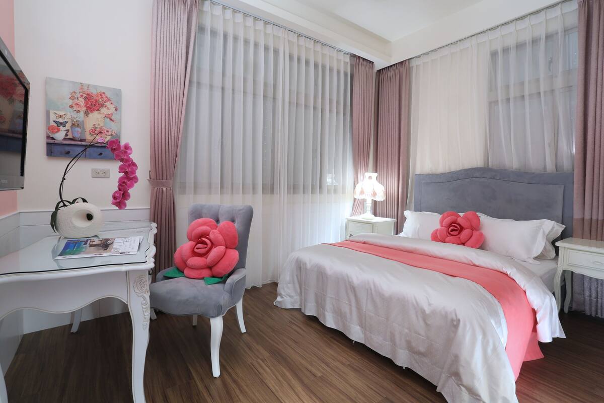Un cuarto de hotel con una cama bien hecha, una silla con un cojín decorativo, un escritorio con una lámpara y un cuadro en la pared.