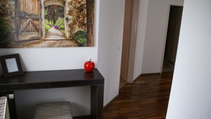 A hallway with wooden flooring, a dark console table with a picture frame and a red apple, and a stone archway with a door. - Moor Apartment (Singen)