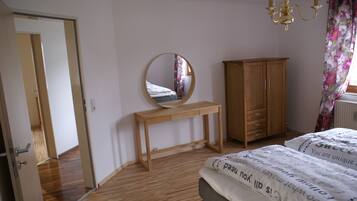 A bedroom with a wooden floor, a bed with a patterned duvet, a wooden bedside table, a mirror, a wardrobe, and a chandelier.