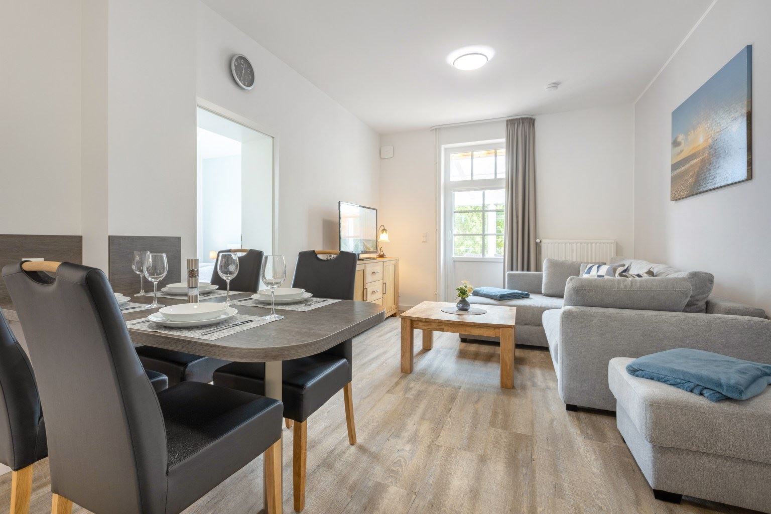 Una sala de estar moderna con comedor, un sofá gris y una mesa de centro de madera.