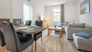 A modern living room with a dining area, a grey sofa, and a wooden coffee table. - Apartment EC right (ID 137) - House Everschop (Sankt Peter-Ording)