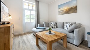 A modern living room with a grey sofa, a wooden coffee table, and a painting on the wall. - Apartment EC right (ID 137) - House Everschop (Sankt Peter-Ording)