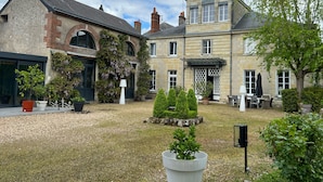 A courtyard with a stone building, a garden with potted plants, and outdoor seating. - Chambres d'hôtes & SPA Les Perce Neige (Vernou-sur-Brenne)
