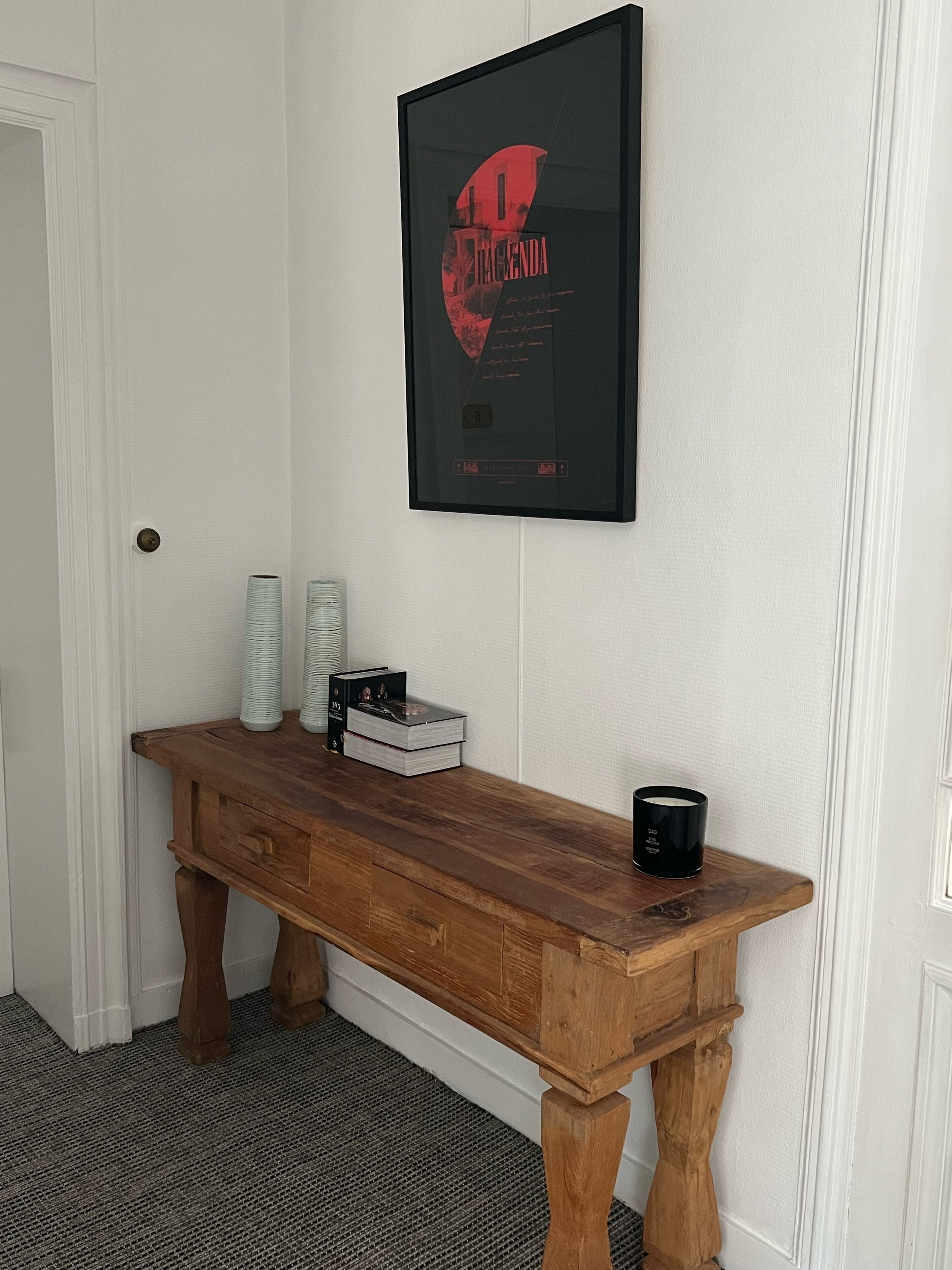 Una consola de madera con un cartel enmarco, una pila de libros y una vela negra.