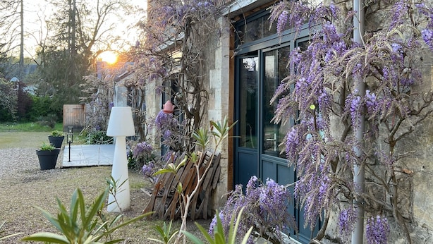 A rustic building with a brick facade, a large window, and purple flowering vines. - Chambres d'hôtes & SPA Les Perce Neige (Vernou-sur-Brenne)