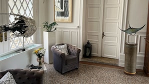 A room with a grey armchair, a decorative metal sculpture, a framed abstract painting, and a white door. - Chambres d'hôtes & SPA Les Perce Neige (Vernou-sur-Brenne)