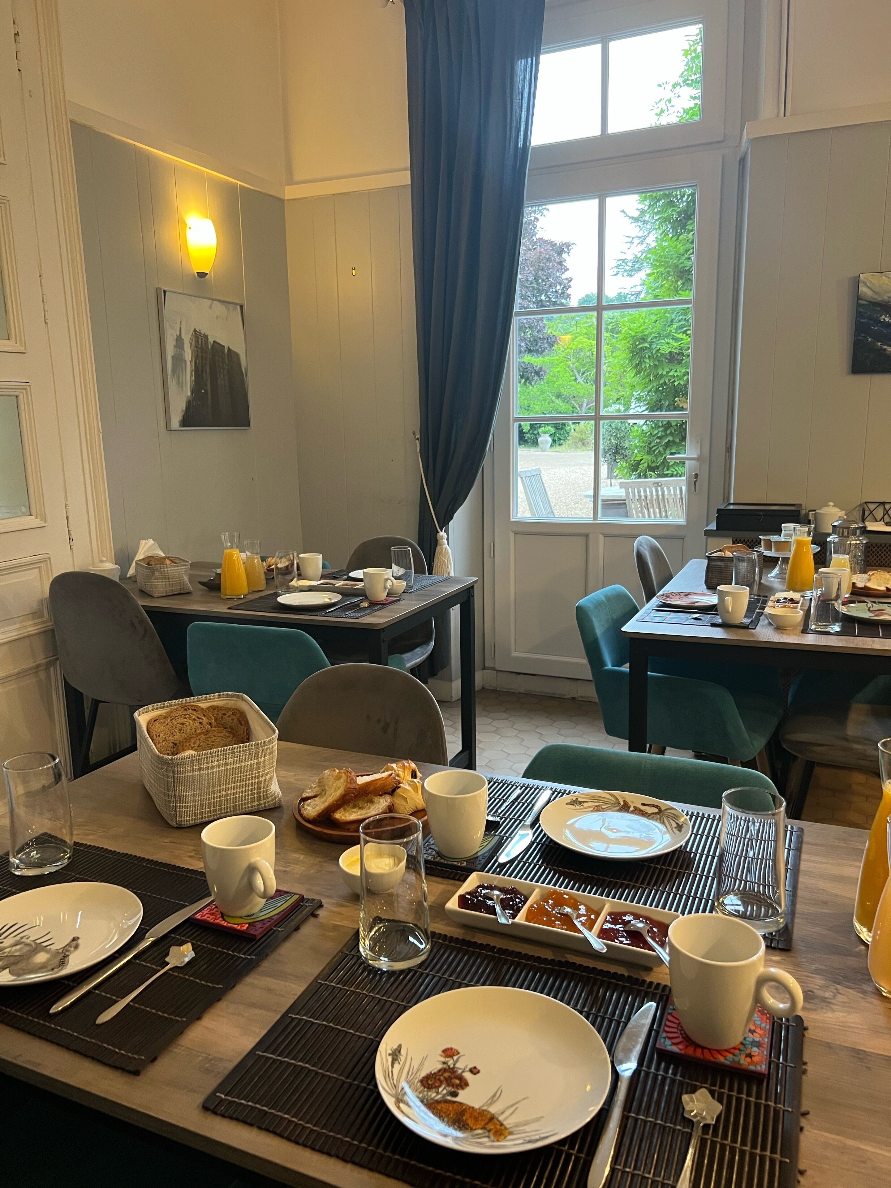 Une table mise pour le petit-déjeuner, avec des couverts pour deux personnes, comprenant des aliments typiques du petit-déjeuner, comme des toasts, des œufs et diverses boissons.