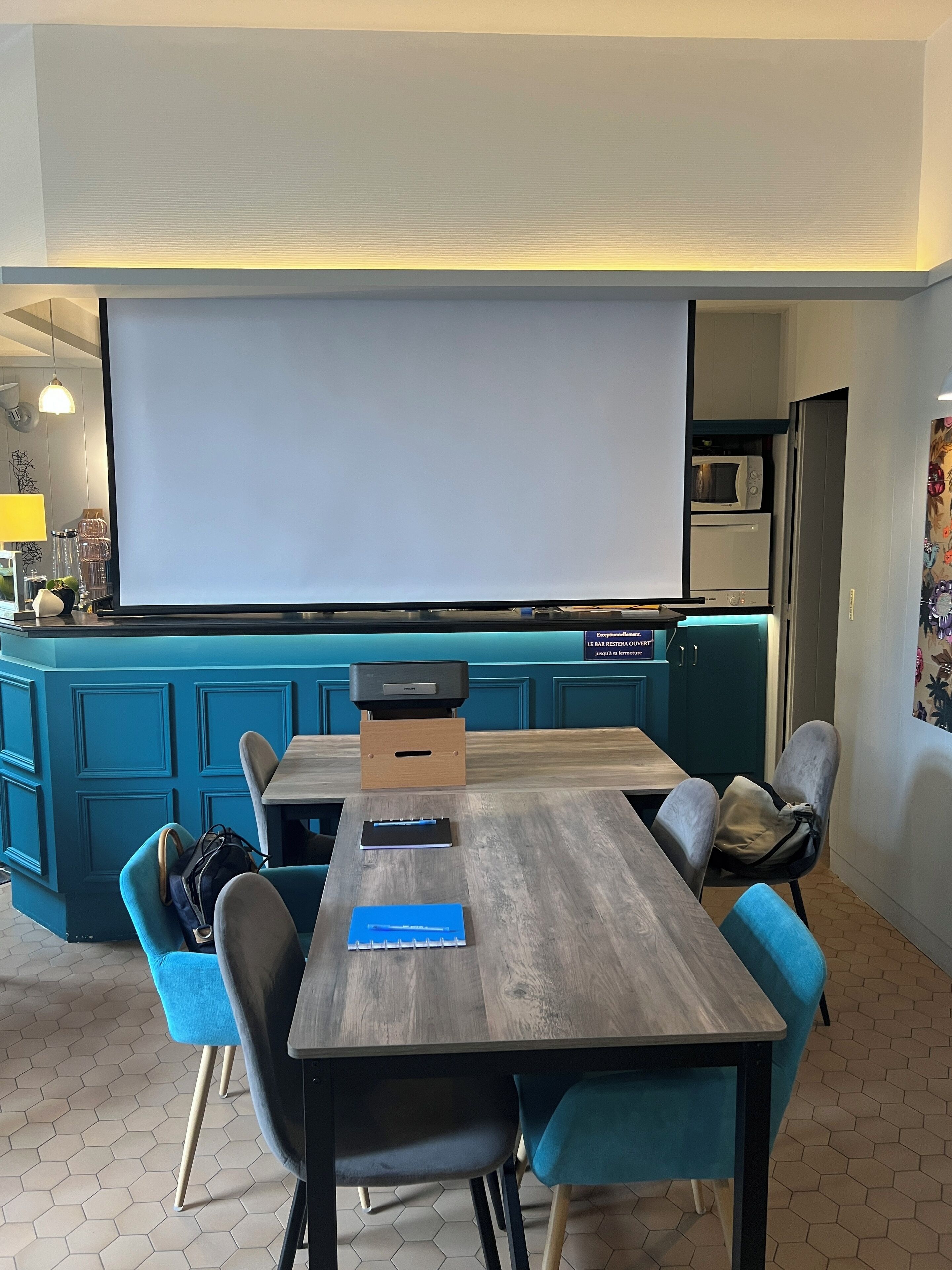 Un salón de conferencias con una pantalla grande, una mesa de madera y sillas azules.