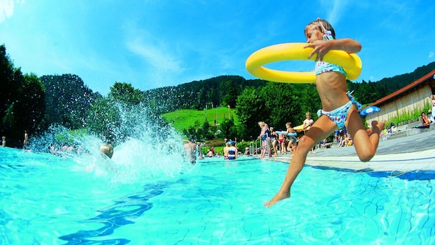 A swimming pool with clear blue water, surrounded by a grassy area and trees. - Ferienwohnung Kaiserstüberl (Reit im Winkl)