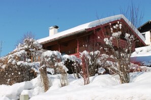 Traditional chalet-style building with a steeply pitched roof, surrounded by snow-covered shrubbery.